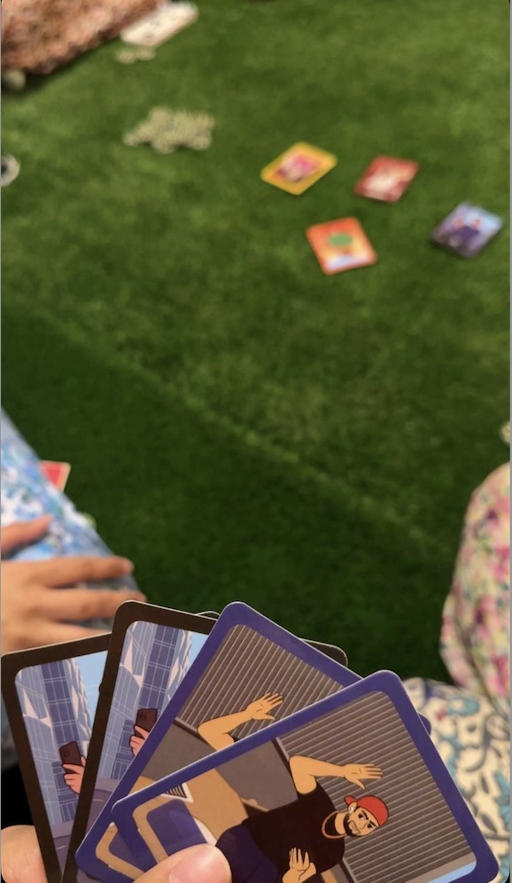 Players holding game cards during an outdoor board game night on artificial grass