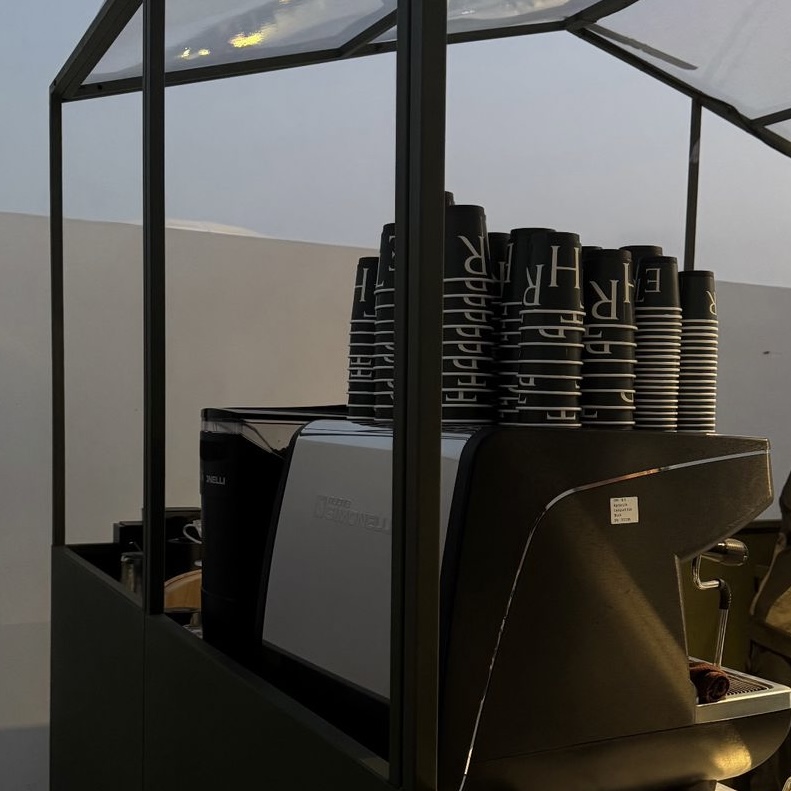 The coffee station featuring a stacked set of cups near the coffee machine. This aesthetic cafe in Abu Dhabi is designed for coffee lovers who enjoy not only great drinks but also the minimalist, sleek vibe of the space