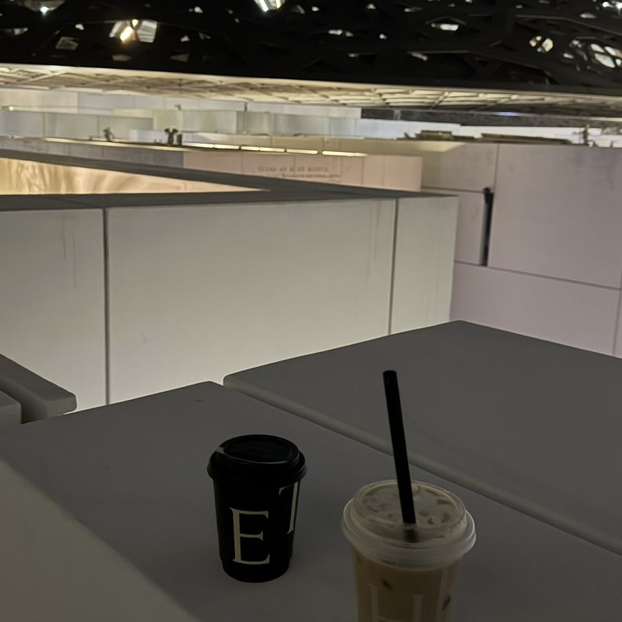 Two refreshing drinks in plastic cups with the Louvre Abu Dhabi in the background. These drinks, served in this Instagrammable cafe in Abu Dhabi, are the perfect pair for a relaxing moment in this modern and aesthetic setting